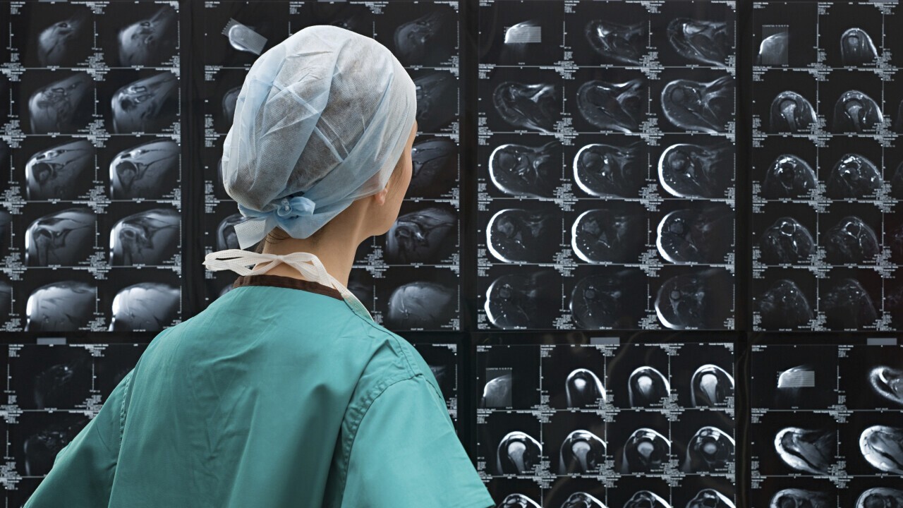 Healthcare professional analyzing a wall of MRI scans. ©Envato